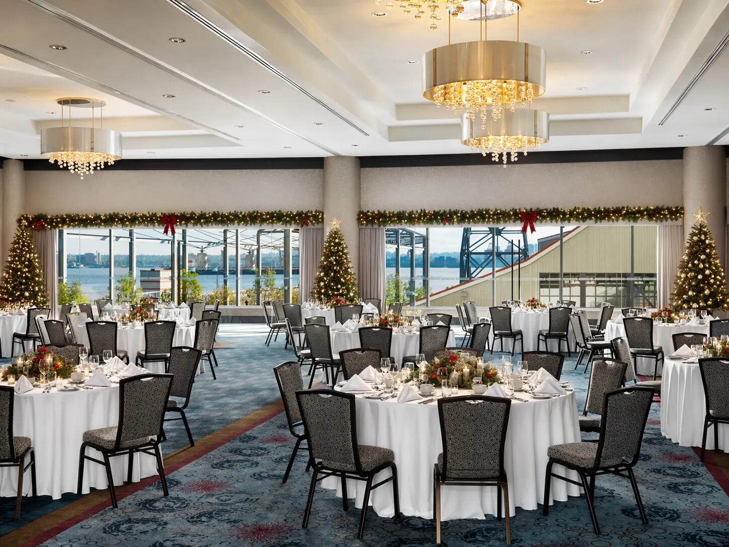 Ballroom set for a festive holiday event with round banquet tables, chandeliers and waterfront views