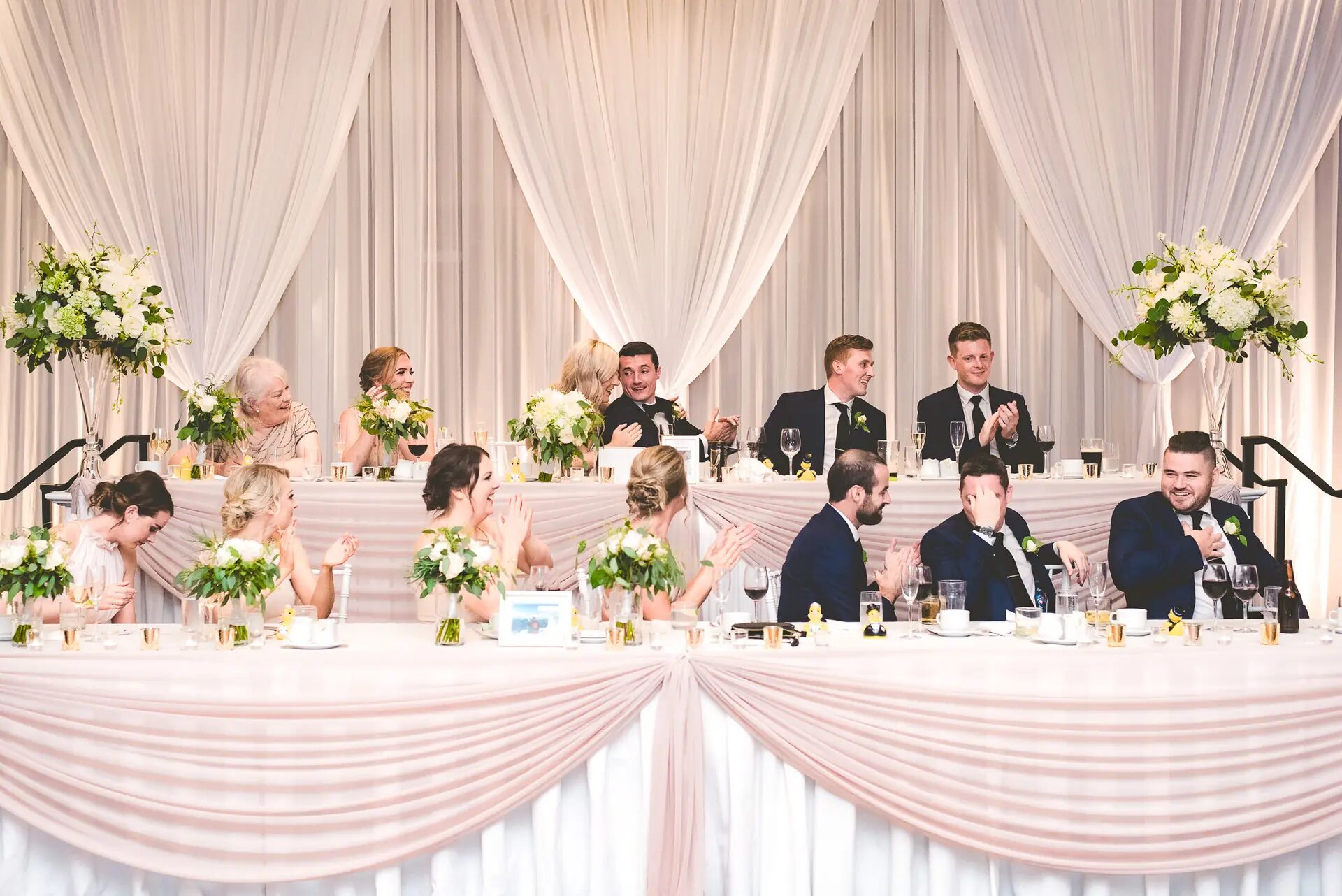 Wedding head table with white and blush draping and lush floral arrangements